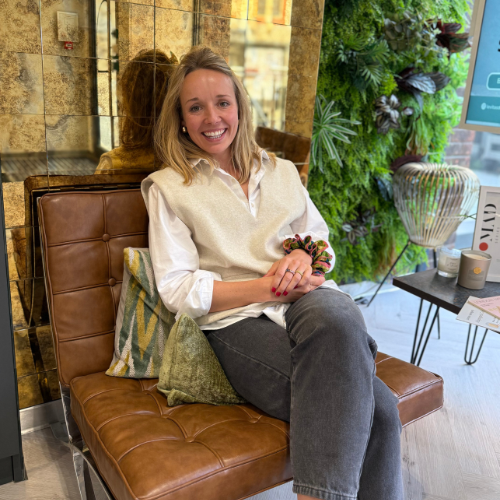 Dr Elizabeth Almas sitting on a tan leather chair in a clinic lounge with a plant wall behind her