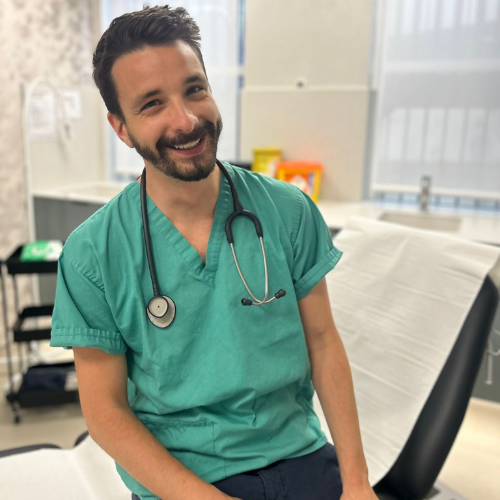 Dr Federico Fedel in green scrubs with a stethoscope, sitting on a treatment couch in a clinic room