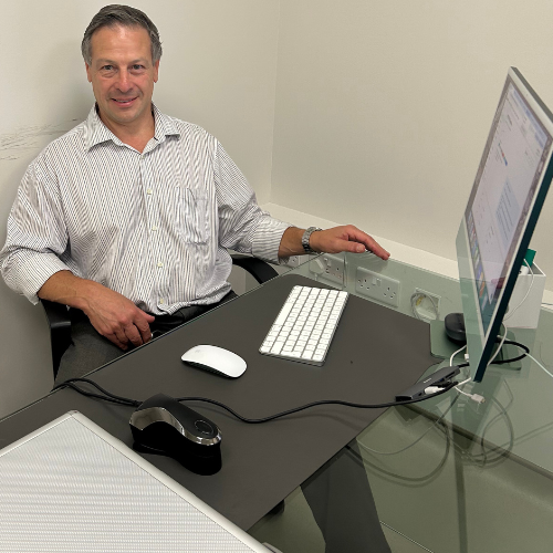 Dr Jonathan Miller sitting at a glass desk with a computer, wearing a striped shirt