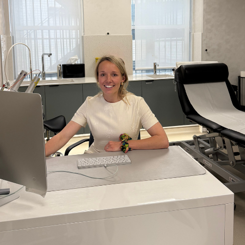 Dr Elizabeth Almas sitting at a desk in a clinic treatment room, wearing a white top