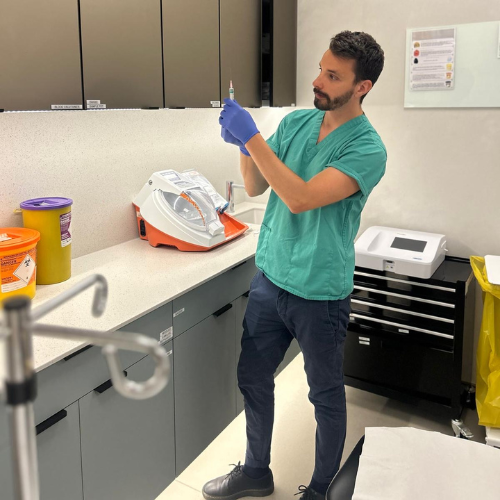 Dr Federico Fedel in green scrubs and blue gloves preparing a syringe in a clinic treatment room