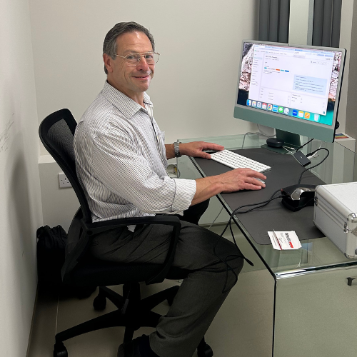 Dr Jonathan Miller, wearing glasses and a striped shirt, working at a computer at a glass desk