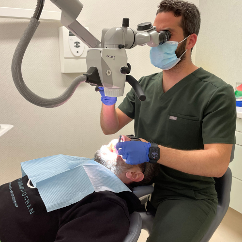 Dr Khaled Elgamaz in dark green scrubs and a face mask, examining a patient’s teeth through a dental microscope