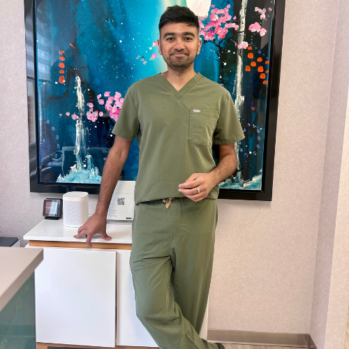 Dr Vijay Prakash in green scrubs, leaning on a cabinet in front of a large colourful painting