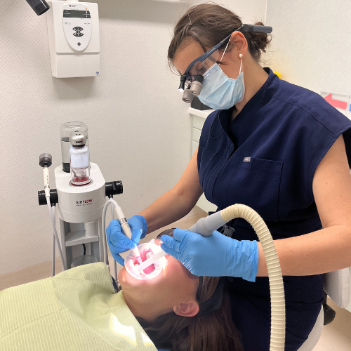 Idalina Silva, wearing loupes and a face mask, treating a patient in a dental chair