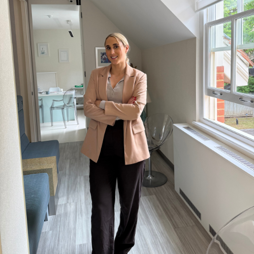 Cara Richardson standing with folded arms in a bright clinic corridor beside a sash window