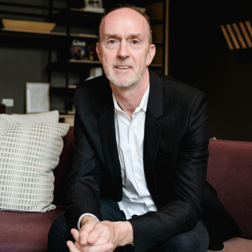 Dr Gareth Morris-Stiff sitting on a sofa with his hands clasped, wearing a dark jacket and a white shirt