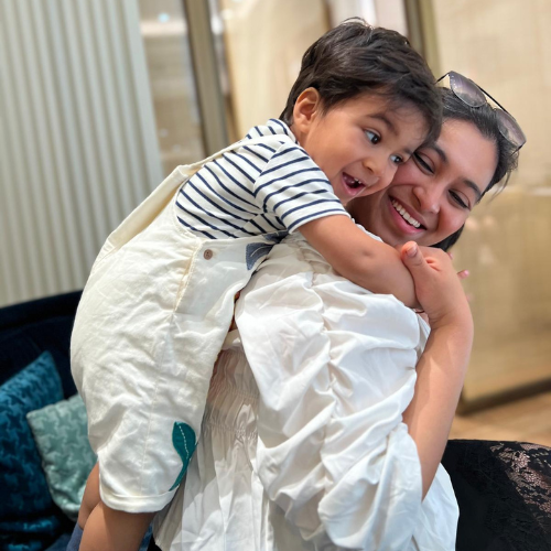 Dr Gunjan Modi laughing as she carries a young child in a striped top on her back