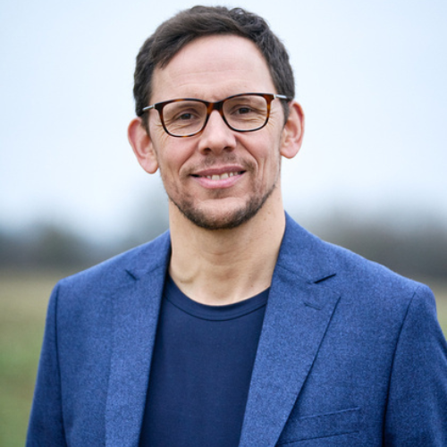 Dr Steve James smiling outdoors, wearing glasses and a blue blazer