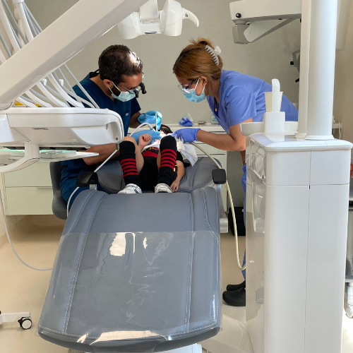 A dentist and a dental nurse in face masks treating a young patient in a dental chair