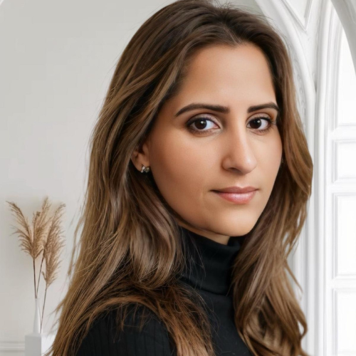Rakhee Mediratta, with long brown hair, wearing a black roll-neck in a bright room with dried pampas grass